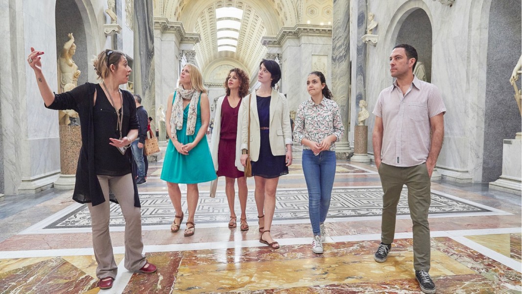 A Context expert guide leading a tour down a marbled hallway in a museum